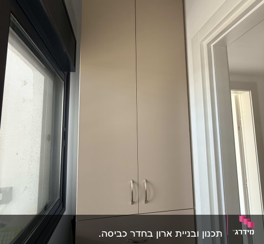 ארון גבוה עם ידיות מתכת ליד חלון ודלת